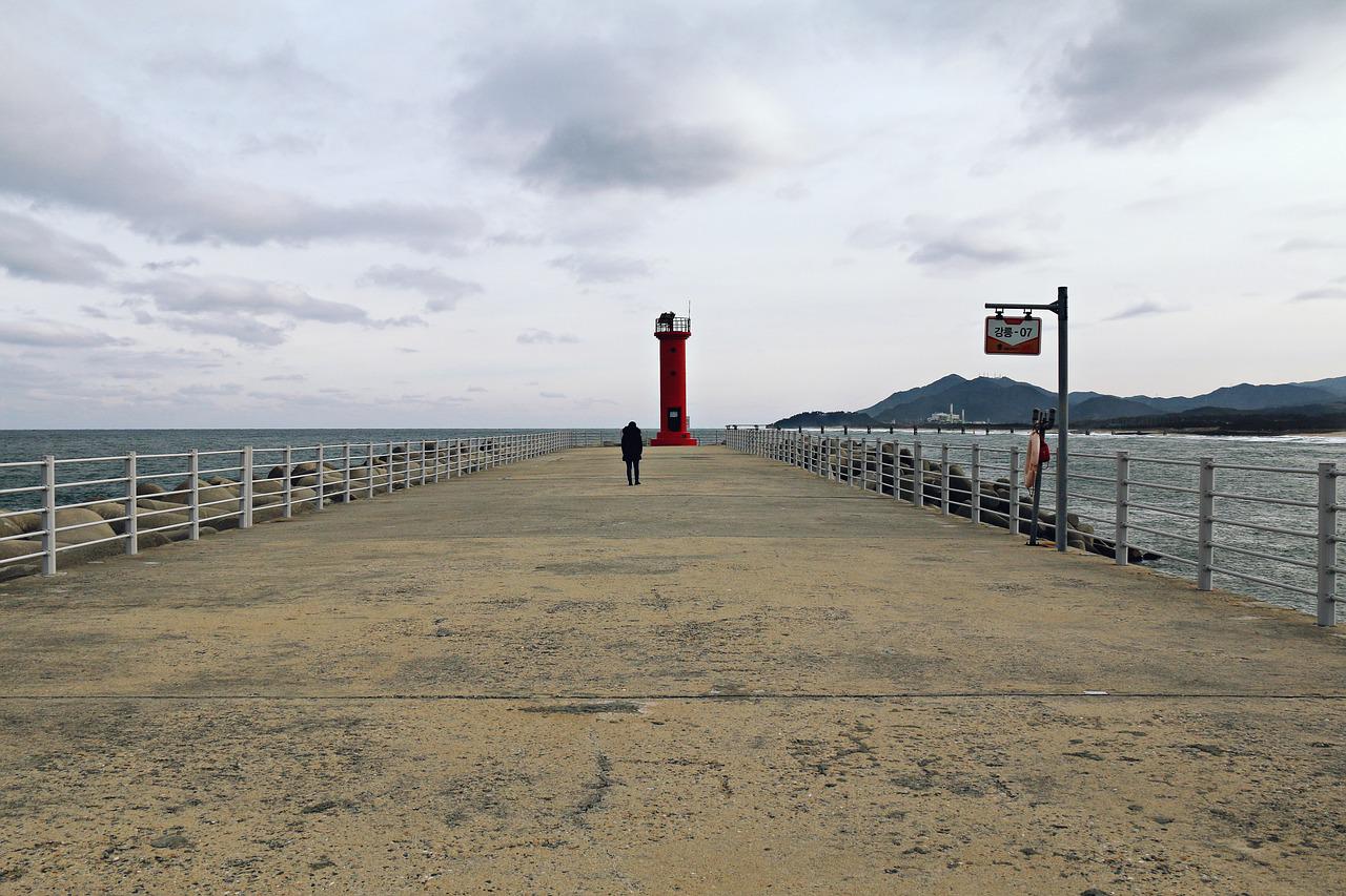 one person walking on deserted pier with lighthouse at end